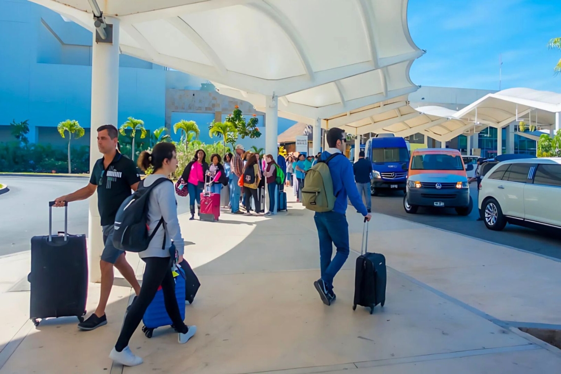 Travelers arriving at Cancun International Airport with luggage and signs for transfers.