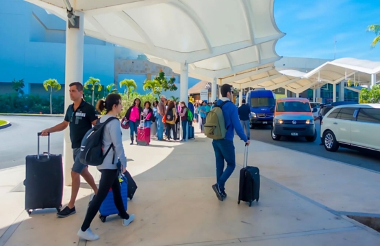 Travelers arriving at Cancun International Airport with luggage and signs for transfers.